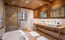 Ein modernes Badezimmer mit Holzverkleidung und zwei Waschbecken. Die Dusche ist durch eine Glasabtrennung getrennt und der Raum ist hell und einladend.