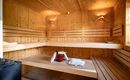 Eine helle Sauna mit Holzregalen und sanftem Licht. Handtücher und ein Holzbehälter stehen bereit.