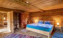 Ein gemütliches Schlafzimmer mitHolzdecke und Wänden. Das Zimmer verfügt über ein großes Bett, einen Stuhl und einen Kleiderschrank.