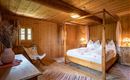 Ein gemütliches Schlafzimmer mit Holzwänden und einem Himmelbett. Der Raum ist warm und einladend, mit sanftem Licht und einfachen Möbeln.