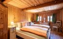 Ein gemütliches Schlafzimmer mit Holzwänden und zwei Betten. Sanfte Beleuchtung und grüne Vorhänge schaffen eine einladende Atmosphäre.