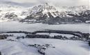 Eine schneebedeckte Landschaft mit hohen Bergen im Hintergrund. Der Himmel ist bewölkt und es gibt Nebel über den Feldern.