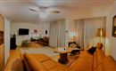 A modern living room with a beige sofa, a coffee table, and a floor lamp. The walls are light, and large windows with curtains provide plenty of daylight.