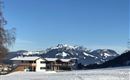 A beautiful winter landscape with snow-covered meadows and impressive mountains in the background. The clear, blue sky completes the scene.