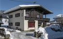 A cozy house in the snow with an upper balcony. The landscape is wintry and the mountains are visible in the background.