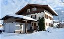 A beautiful two-story house with a gabled roof, surrounded by snow. The sky is clear with some clouds.