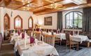 Ein gemütliches Restaurant mit elegant eingedeckten Tischen und Holzdecke. Große Fenster sorgen für angenehmes Licht und eine einladende Atmosphäre.