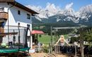An idyllic house with a garden and playground, surrounded by majestic mountains.  
Children are happily playing on the swing and trampoline.