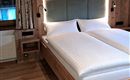 Ein gemütliches Schlafzimmer mit einem Doppelbett und hellem Holzinterieur. Die Wände sind mit dezenten Vorhängen und modernen Lampen dekoriert.