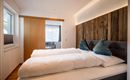 Ein modernes Schlafzimmer mit zwei Einzelbetten und stilvollen Kissen. Die Wände sind teilweise mit Holz verkleidet, und viel Tageslicht strömt durch das Fenster.