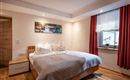 Ein modernes Schlafzimmer mit einem großen Bett und hellen Wänden. Ein Fenster mit Vorhängen und ein Bild an der Wand sorgen für eine gemütliche Atmosphäre.