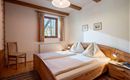 Ein gemütliches Schlafzimmer mit zwei Betten und farbenfrohen Bettwäsche. Ein Fenster mit Pflanzen und sanftem Licht sorgt für eine einladende Atmosphäre.