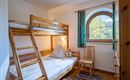 Ein gemütliches Zimmer mit einem Etagenbett und einem einzelnen Stuhl. Große Fenster bieten einen Blick auf die Natur draußen.