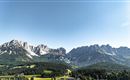 An impressive mountain landscape with high peaks and a clear sky. The green meadow in the foreground complements the picturesque panorama.