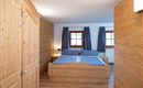 A cozy bedroom with wood paneling and a double bed. Large windows and curtains create a bright atmosphere.