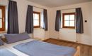 A bright bedroom with two windows and blue curtains. The bed is neatly covered with blue bed spreads.