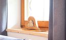 A wooden heart with a creative pattern of small sticks stands on a windowsill. In the background, curtains and a window can be seen.