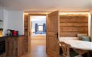 A cozy apartment with wood paneling and modern kitchen equipment. The room is bright and inviting, with access to a bedroom.