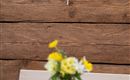 A small table with a vase full of flowers is in a rustic room. A key is hanging on a small sign on the wall.