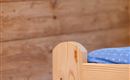A part of a wooden bed frame with a blue bedspread. In the background, a wooden wall is visible.