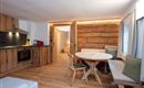A cozy living kitchen made of wood with modern furnishings. The room has a round table and a comfortable seating area.
