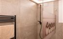 A modern bathroom with a glass shower cabin and a stylish wall covering. The room is decorated in neutral tones and features soft lighting.