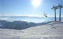 Eine wunderschöne Winterlandschaft mit schneebedeckten Bergen. Skilifte sind im Vordergrund, und die Sonne strahlt am klaren Himmel.