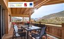 Eine einladende Terrasse mit einem Tisch und Stühlen, umgeben von malerischen Bergen. Die Holzstruktur verleiht der Umgebung eine warme und gemütliche Atmosphäre.