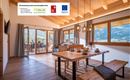 Ein modernes Esszimmer mit Holzinterior und großen Fenstern. Der Tisch ist gedeckt und bietet einen Blick auf die umliegenden Berge.