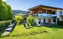 A modern house with a large garden and a terrace. The surroundings are green and hilly, ideal for relaxation.
