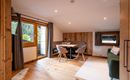 A cozy living space with a dining table, bright walls, and large windows. The room is decorated with modern furniture and wooden elements.