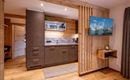 A modern kitchen with wood paneling and stylish appliances. A television displays a mountain landscape on the wall.