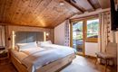 A cozy bedroom with a large double bed and wooden beam ceiling. Through the window, one looks out onto a green landscape.