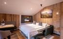A cozy bedroom with wooden paneling and a double bed. There is a small dining area and a window with a view of the mountains.