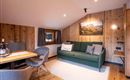 A cozy living room with a green sofa and a dining area. The walls are clad in wood and a picture of a mountain landscape hangs on the wall.