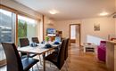 Eine modern eingerichtete Wohnung mit einem Essbereich und einem großen Fenster. Der Tisch ist gedeckt, und es gibt einen Fernseher sowie gemütliche Sitzgelegenheiten.