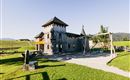 A playground in the shape of a castle with a large tower and swings. The surroundings consist of green grass and a clear blue sky.