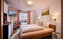 Ein gemütliches Schlafzimmer mit einem Doppelbett und dekorativen Kissen. Es gibt eine kleine Küchenzeile und Balkon mit Blick auf die Berge.