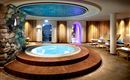 An elegant wellness area with a round hot tub in the center.  
Surrounded by comfortable loungers and warm light, this space invites relaxation.