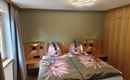 Een knusse slaapkamer met een tweepersoonsbed en bloemen decoratie op het beddengoed. De muren zijn in zachte kleuren gehouden, en er zijn moderne lampen naast het bed.