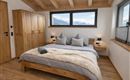 Ein modernes Schlafzimmer mit einem großen Bett und Holzdekor. Große Fenster bieten einen Blick auf die Berge.
