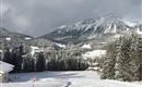 A snow-covered mountain landscape with tall fir trees and majestic mountains in the background. The atmosphere is calm and inviting.