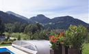 Ein schöner Ausblick auf Berge und grüne Wiesen. Im Vordergrund stehen blühende Pflanzen und ein Pool mit einer Abdeckung.