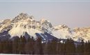 Eine beeindruckende Berglandschaft mit schneebedeckten Gipfeln und einem klaren Himmel. Die Wälder im Vordergrund vervollständigen das malerische Bild.