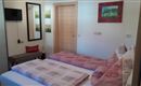 A cozy bedroom with two beds and red pillows. On the wall hang pictures and a mirror, there is a small television and a wooden door.