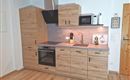 A modern kitchen made of wood with a countertop and a stove. It features a refrigerator and a microwave, as well as an elegant sink.