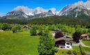 A picturesque landscape with green meadows and mountains in the background. Here are some buildings and trees that create a peaceful atmosphere.