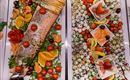 A lavish buffet featuring grilled salmon, fresh sides such as tomatoes and citrus fruits. On the other side, there are attractively decorated platters with fruits and delicious small bites.