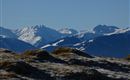 Schneebedeckte Berge unter klarem blauen Himmel. Sanfte Hügel im Vordergrund ergänzen die alpine Landschaft.