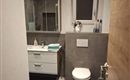 Ein modernes Badezimmer mit einer weißen Toilette und einem Waschbecken. Der Boden ist grau und es gibt einen blauen Teppich.
